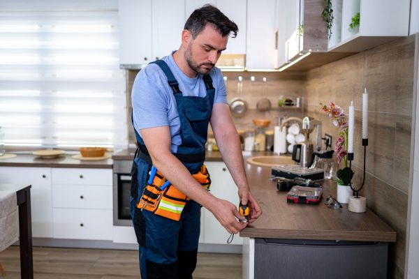 A worker focuses on repairs in a bright kitchen, surrounded by tools and equipment.