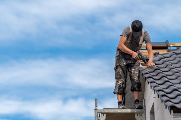 the craftsman screws a ceramic tile onto the wooden beams of the roof. banner